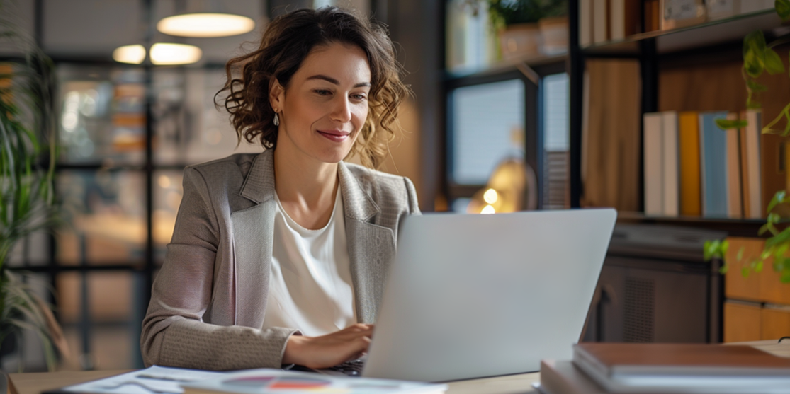 Woman in a blazer working on a laptop in a modern office.